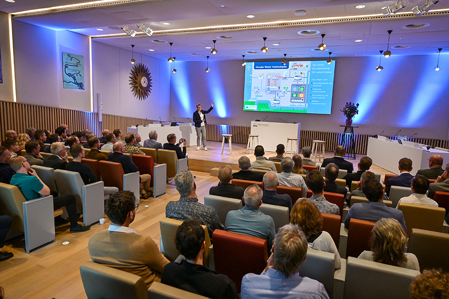 Vrouw presenteert op podium aan volle zaal.