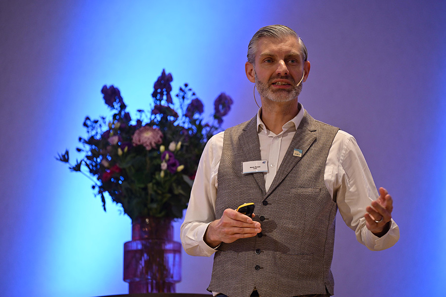 Man staat op podium en gebaart met zijn hand naar voren.