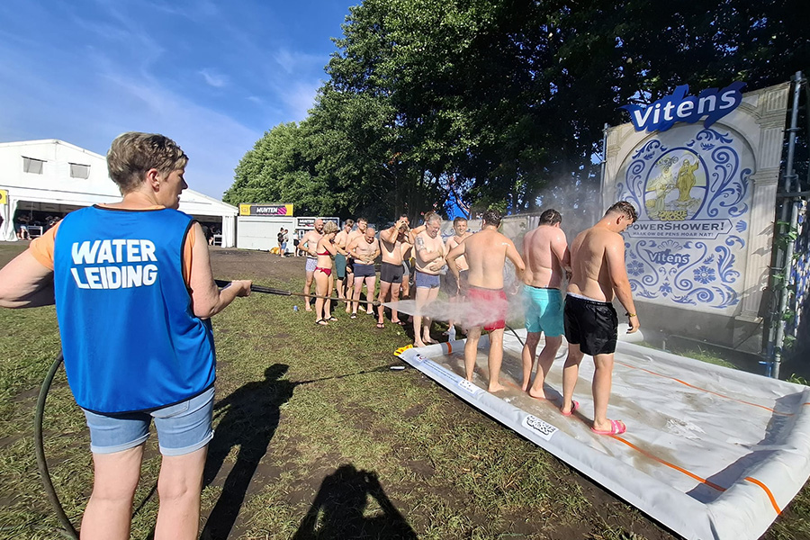Medewerker van Vitens spoelt festivalgangers af.