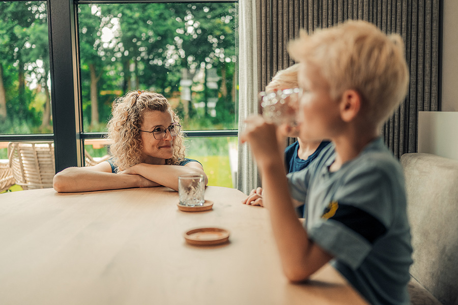 Moeder zit aan tafel met twee jongetjes die een glas water drinken
