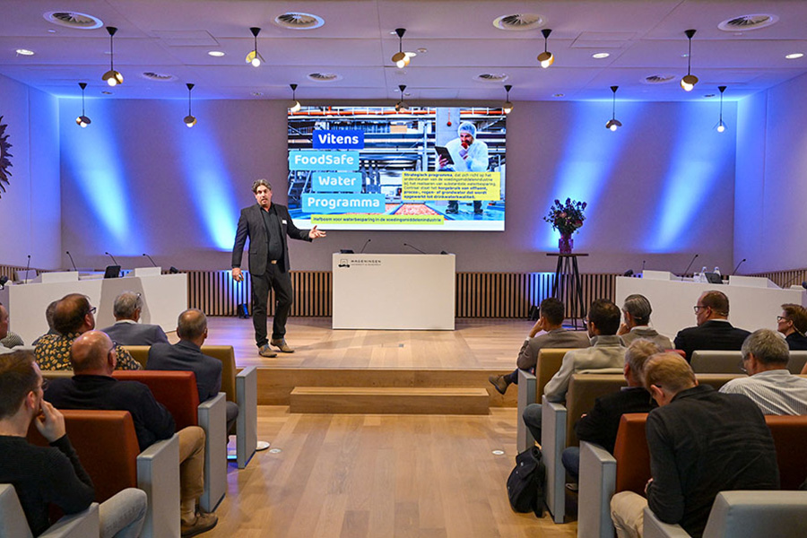 Man staat op podium met achter zich een diascherm met de tekst Vitens FoodSafe Water Programma.