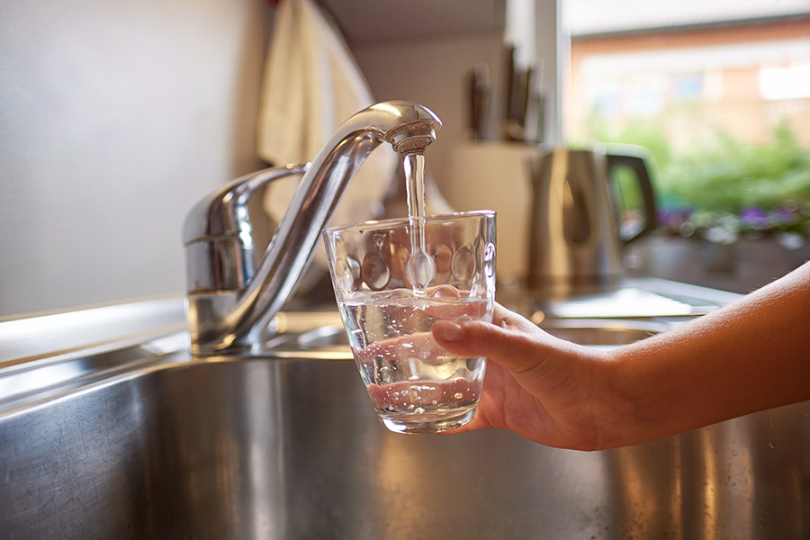 Hand vult glas water onder de keukenkraan.